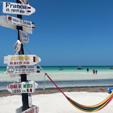 Holbox, Mexique Panneaux directionnels sur une plage, avec des hamacs et un ciel bleu.