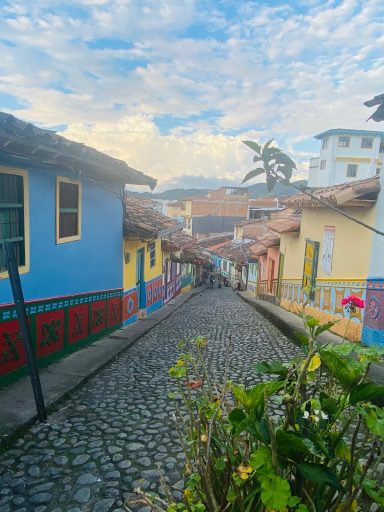 Guatapé, Colombie Rue en pente avec des maisons colorées et des pavés sous un ciel nuageux.