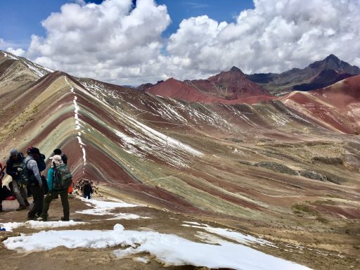 Vinicunca, Montagne aux 7 couleurs Randonneurs sur un sommet avec des montagnes colorées sous un ciel nuageux.