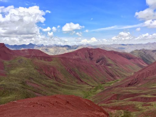 Vallé rouge Pérou Vue panoramique de montagnes rougeâtres sous un ciel nuageux avec des vallées verdoyantes.