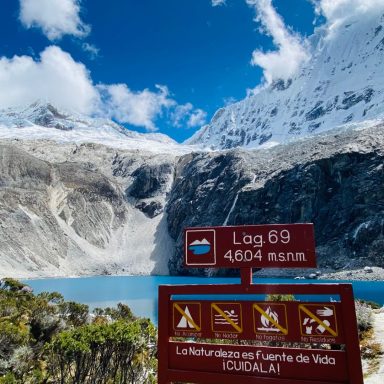 Pérou, Lac 69, laguna 69 Vue d'un lac turquoise en montagne, avec un panneau d'information et des sommets enneigés.