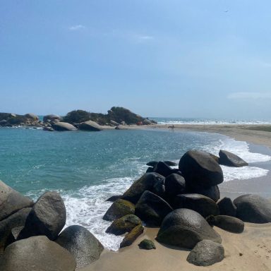 Parc Tayrona Plage tranquille avec des rochers et des vagues scintillantes sous un ciel clair.