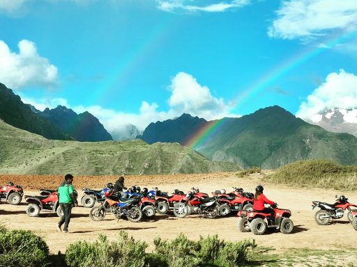 Marras Morray - Quad - cusco Des personnes en quad près d'une montagne, avec un arc-en-ciel dans le ciel clair.